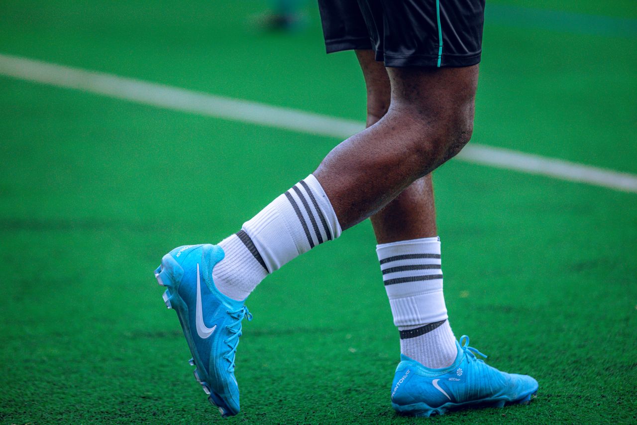 About A soccer player's legs and feet in action on a green field wearing blue cleats.